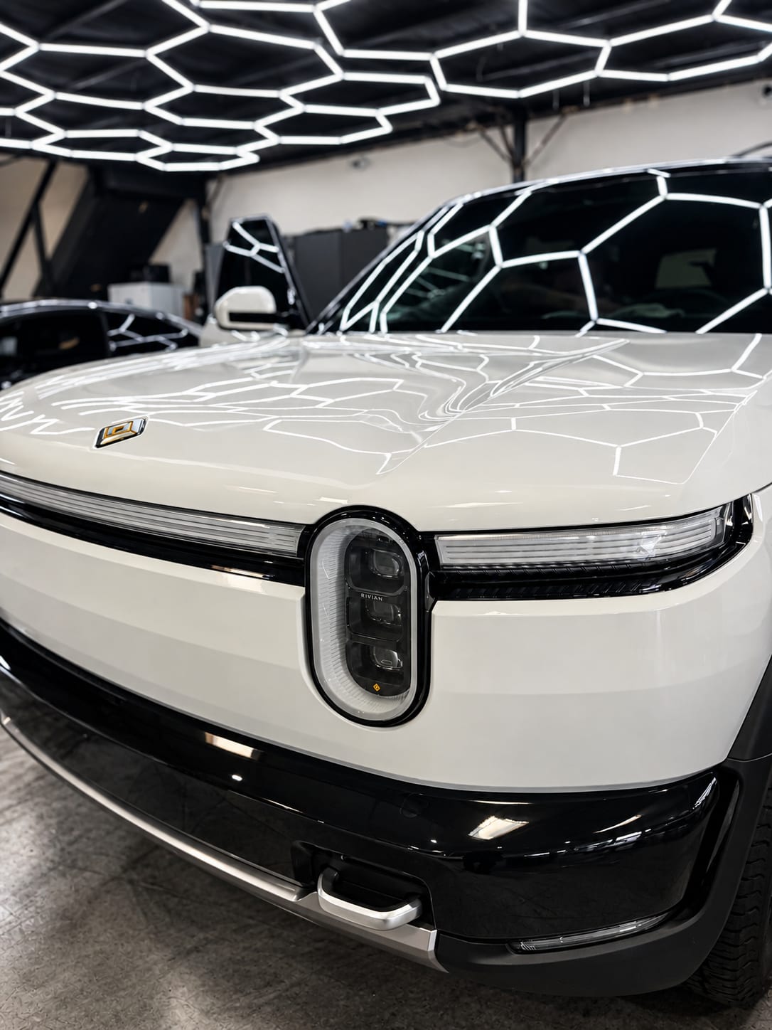 rivian r2 paint protection — close-up of the Rivian R2 hood and headlight reflecting the shop lights after ceramic coating